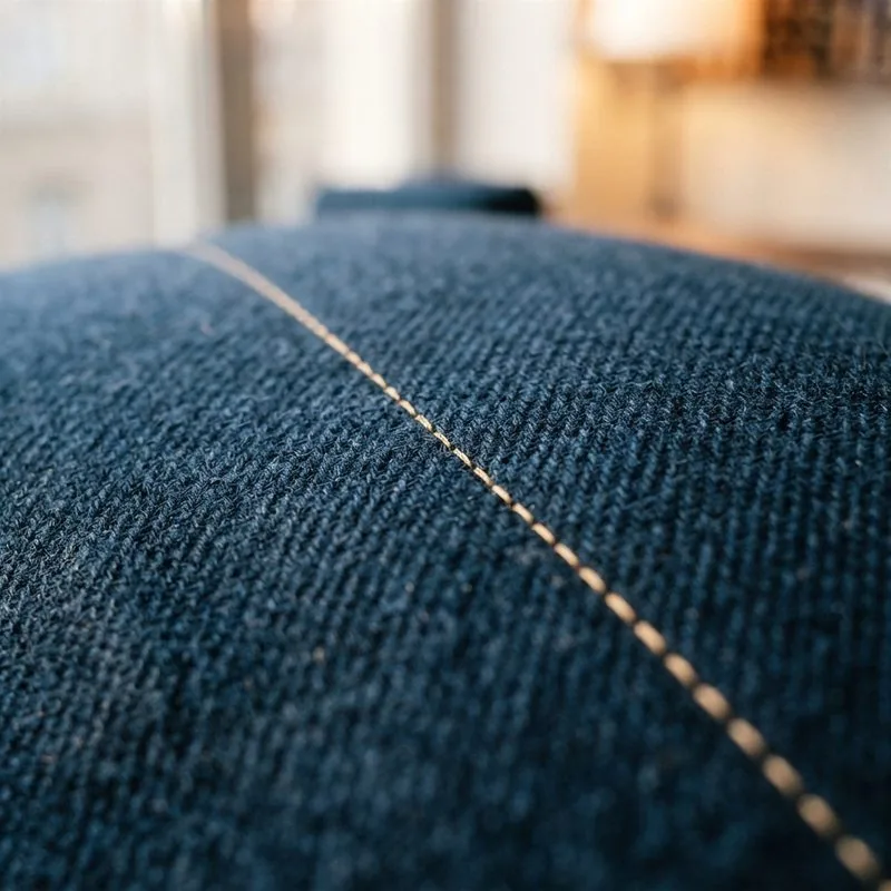 Nahaufnahme einer sauberen Steppnaht in Goldbeige auf marineblauem Wollstoff.